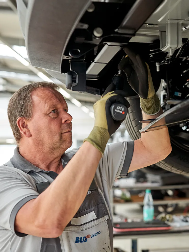 Handwerker schraubt an der unterseite eines Fahrzeugs (Foto)