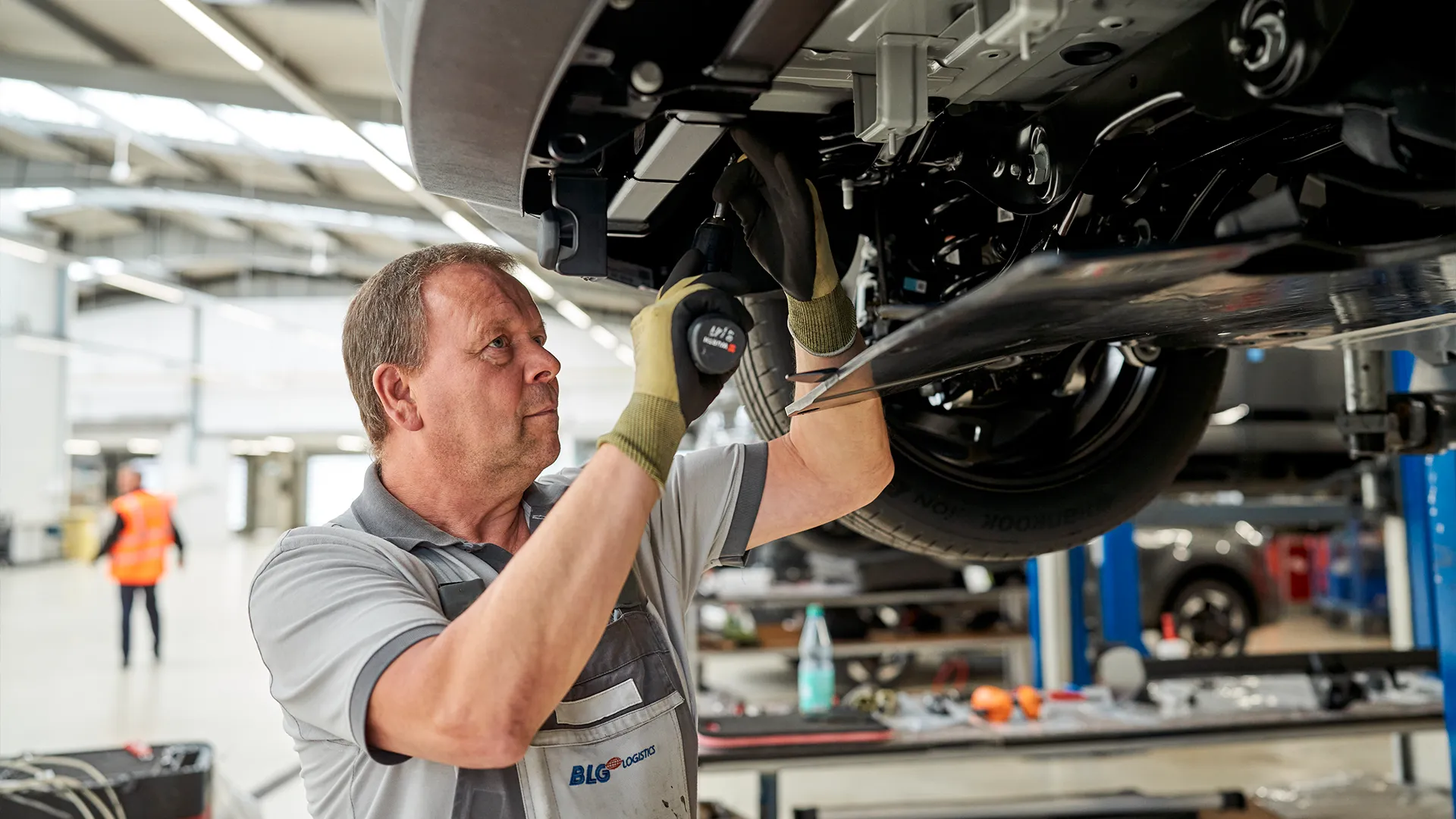 Handwerker schraubt an der unterseite eines Fahrzeugs (Foto)