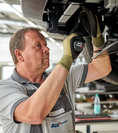 Vorschaubild, Handwerker schraubt an der unterseite eines Fahrzeugs (Foto)