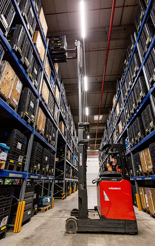 Red forklift moving between tall warehouse shelves in a storage facility