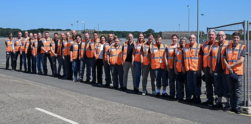 Group photo of employees outdoors wearing orange vests, preview (Photo)