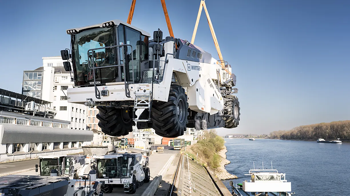 Heavy road milling machine being lifted over a river by crane (Photo)